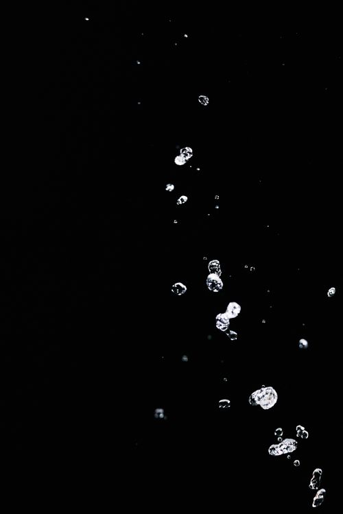 Free Close-up of water droplets captured mid-air against a stark black background, highlighting fluid motion and texture. Stock Photo