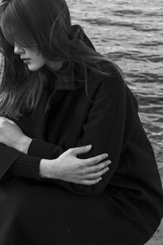 Black and white portrait of a woman with long hair sitting by water, arms crossed.