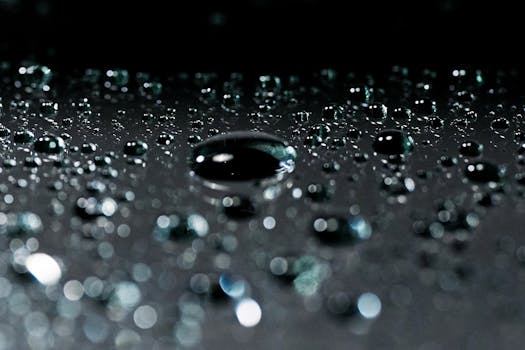 Detailed shot of water droplets on a dark reflective surface, showcasing texture and reflection.
