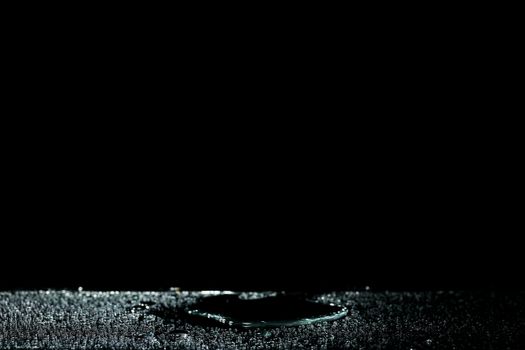 Moody and artistic composition of water droplets on a shiny surface against a black background.