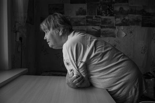 Grayscale Photo of an Elderly Woman Leaning on Table