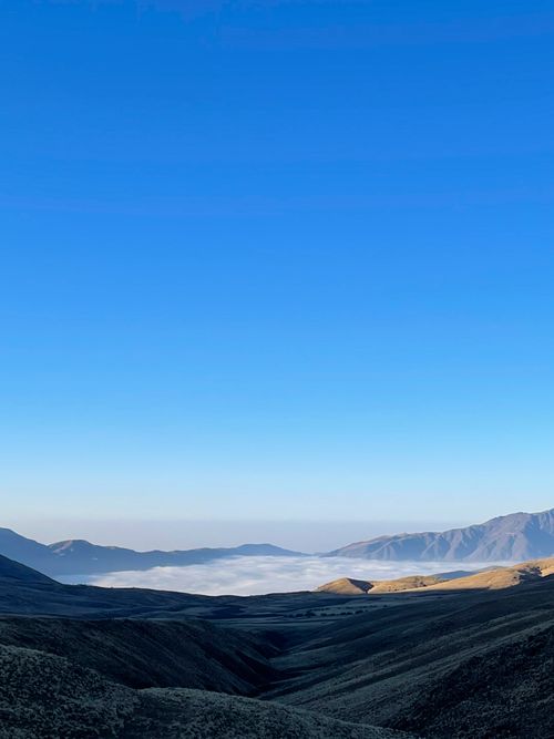 Free A scenic view of a mountain valley under a vast blue sky with low clouds. Stock Photo