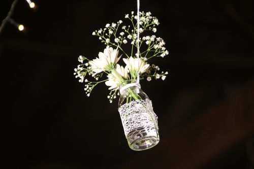 Free Delicate white flowers in a lace-wrapped glass bottle suspended against a dark backdrop. Stock Photo