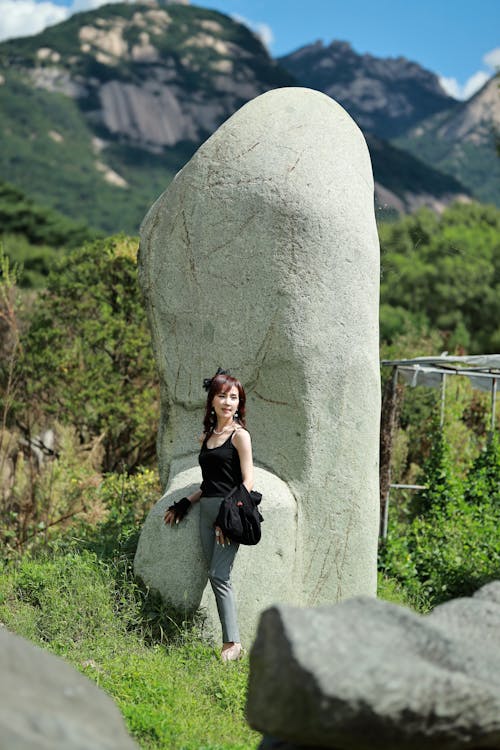 A Woman in Black Tank Top and Gray Pants Standing Beside a Boulder