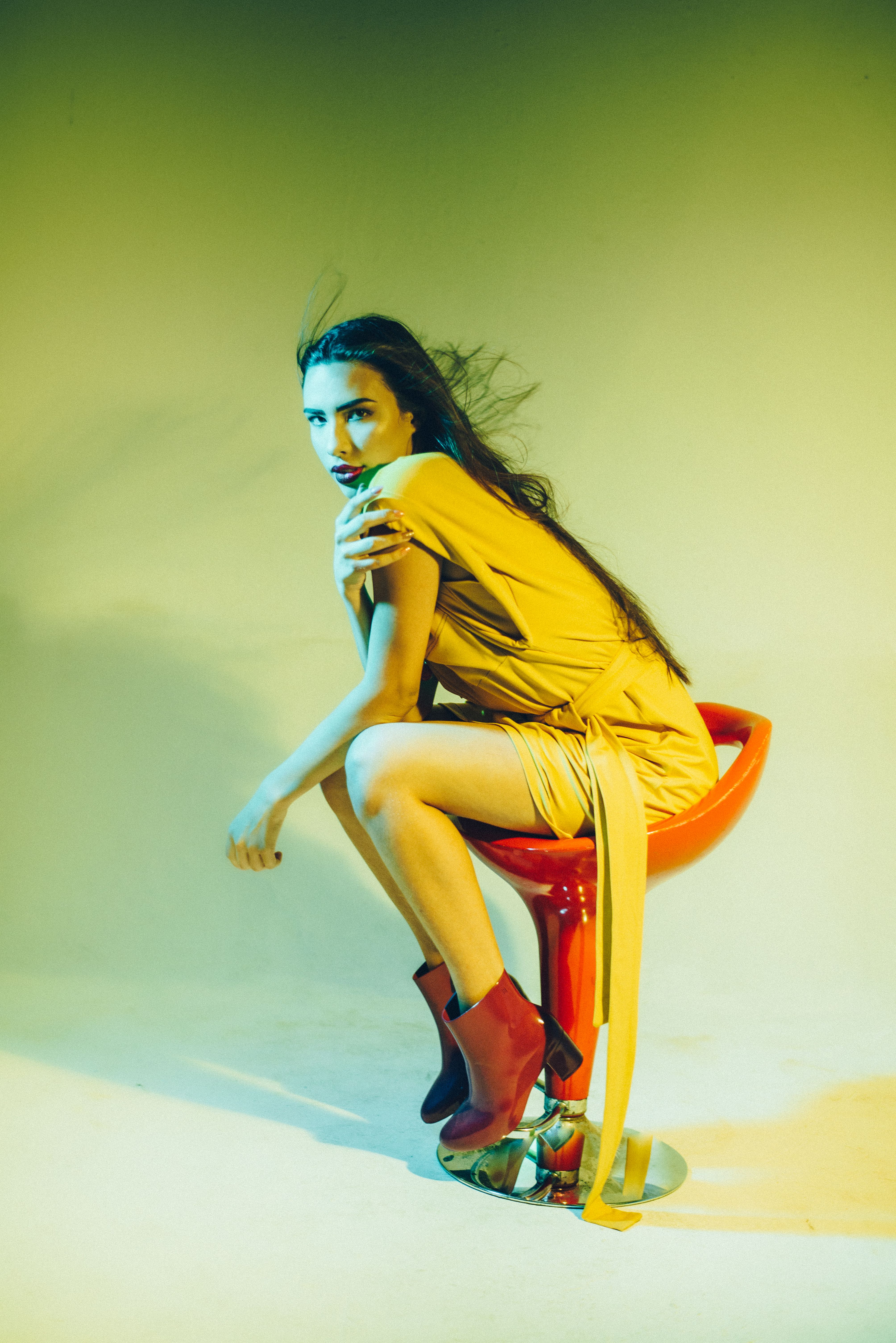 A striking artistic portrait of a woman in a yellow dress posing on a red chair, captured with a dramatic lighting effect.
