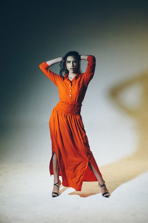 Free Sophisticated portrait of a woman in an elegant orange dress, captured in a studio setting with moody lighting. Stock Photo