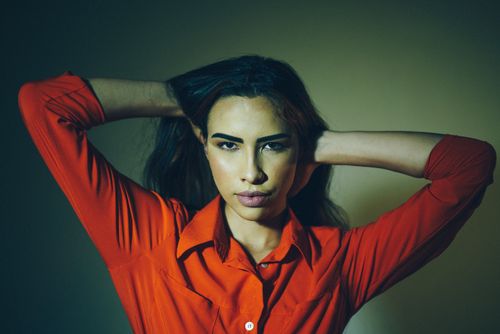 Free Striking portrait of a woman with hands on head, wearing a vibrant red shirt. Studio lighting enhances dramatic mood. Stock Photo