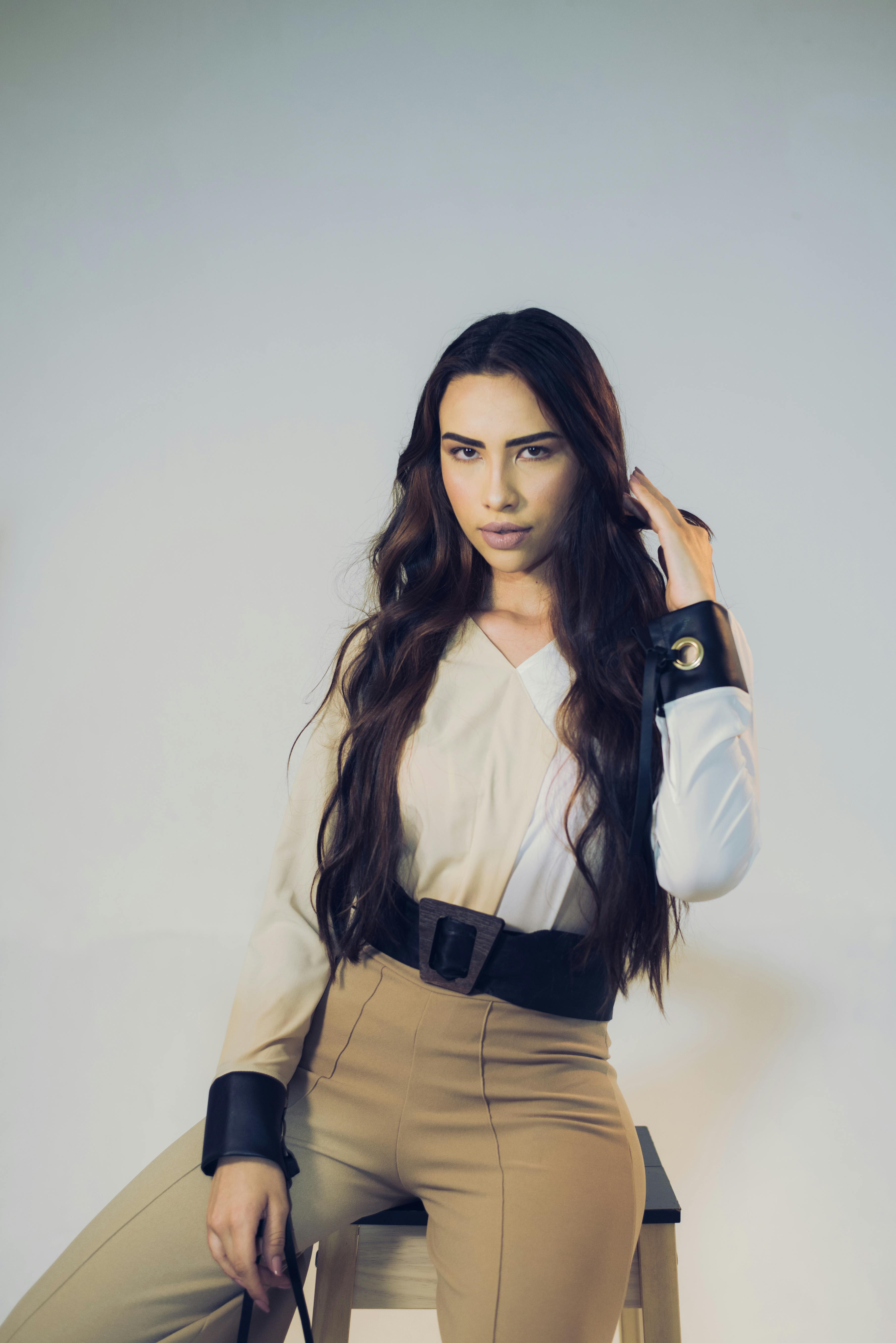 Free Elegant woman with long hair sitting on a stool in stylish fashion outfit. Stock Photo