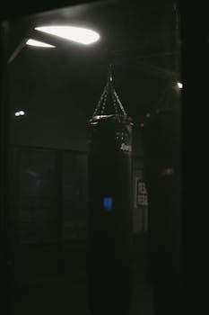 Dark gym interior featuring a hanging punching bag under soft lighting.
