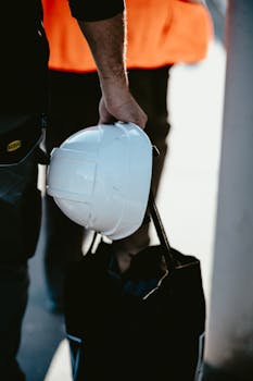 A close-up of a worker holding a white safety helmet, emphasizing safety and professionalism.