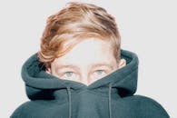 一个躲在深色连帽衫里的小男孩，肖像高调地突出了他的眼睛