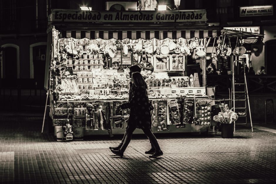 Una pareja pasa por un puesto de mercado iluminado por la noche, vendiendo varios productos.