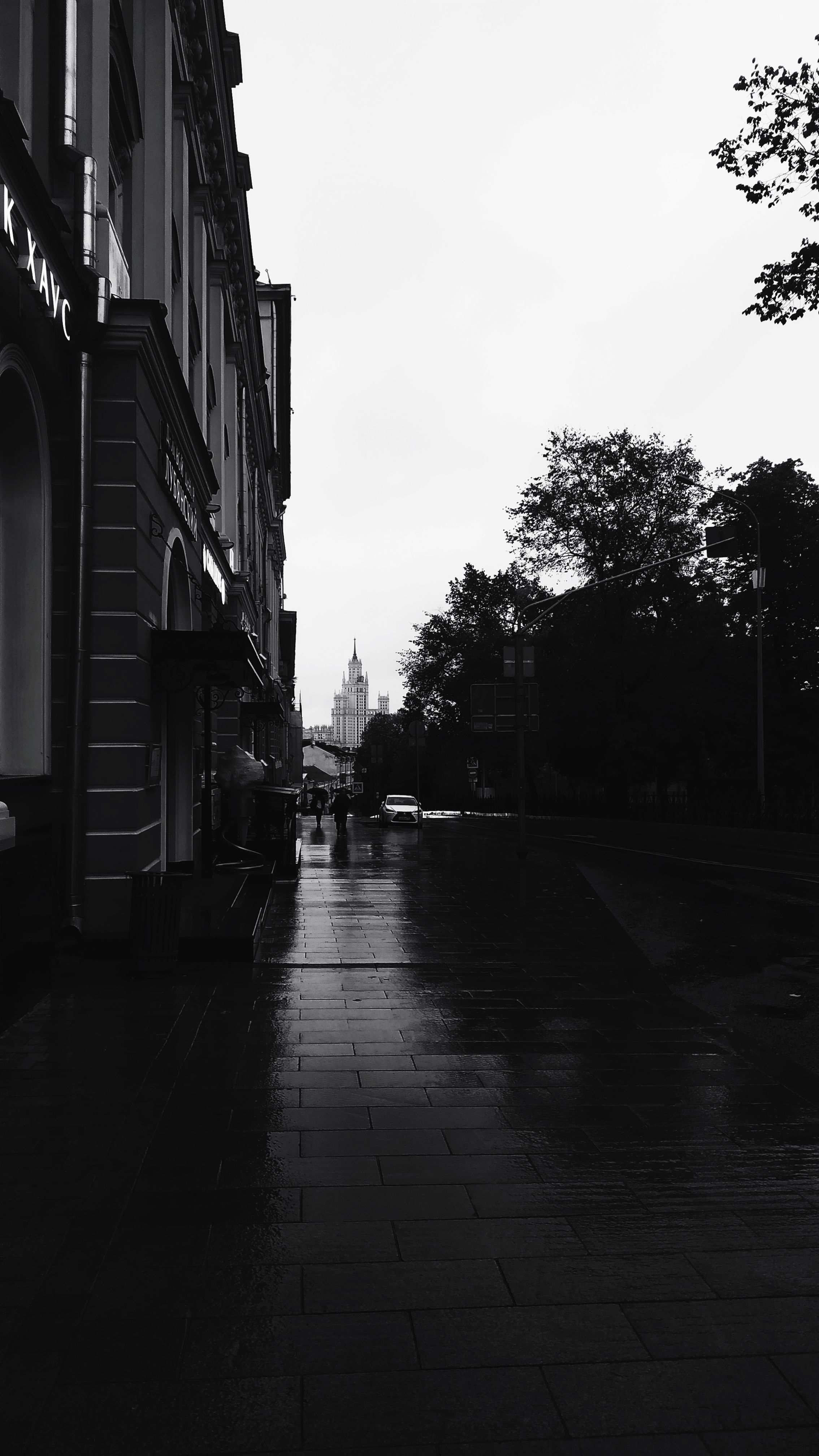 Black and white photo of a rainy street, highlighting architecture and reflections.