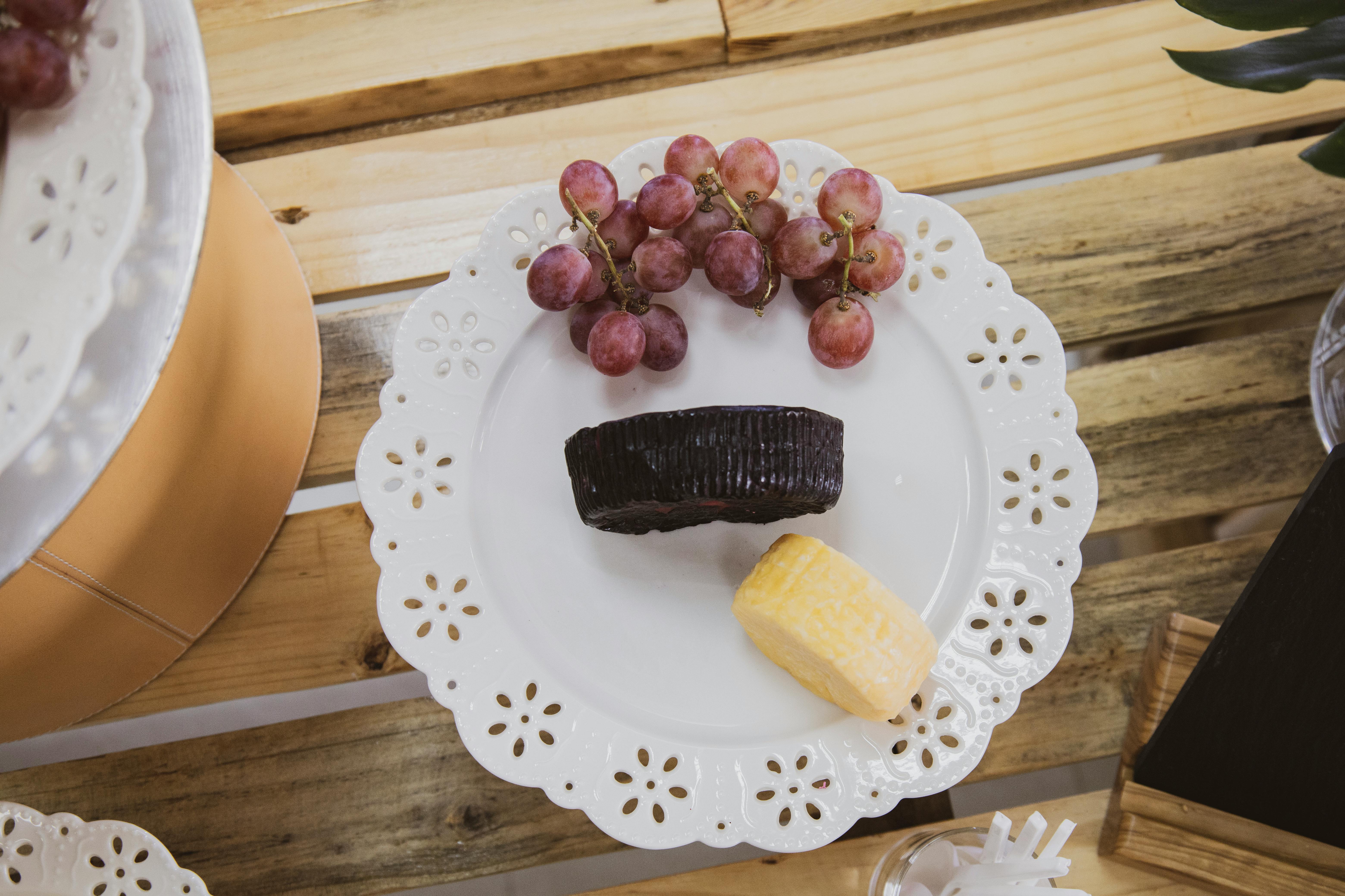 A top-down view of cheese and grapes on a decorative plate on a rustic wood table, perfect for gourmet food presentations.