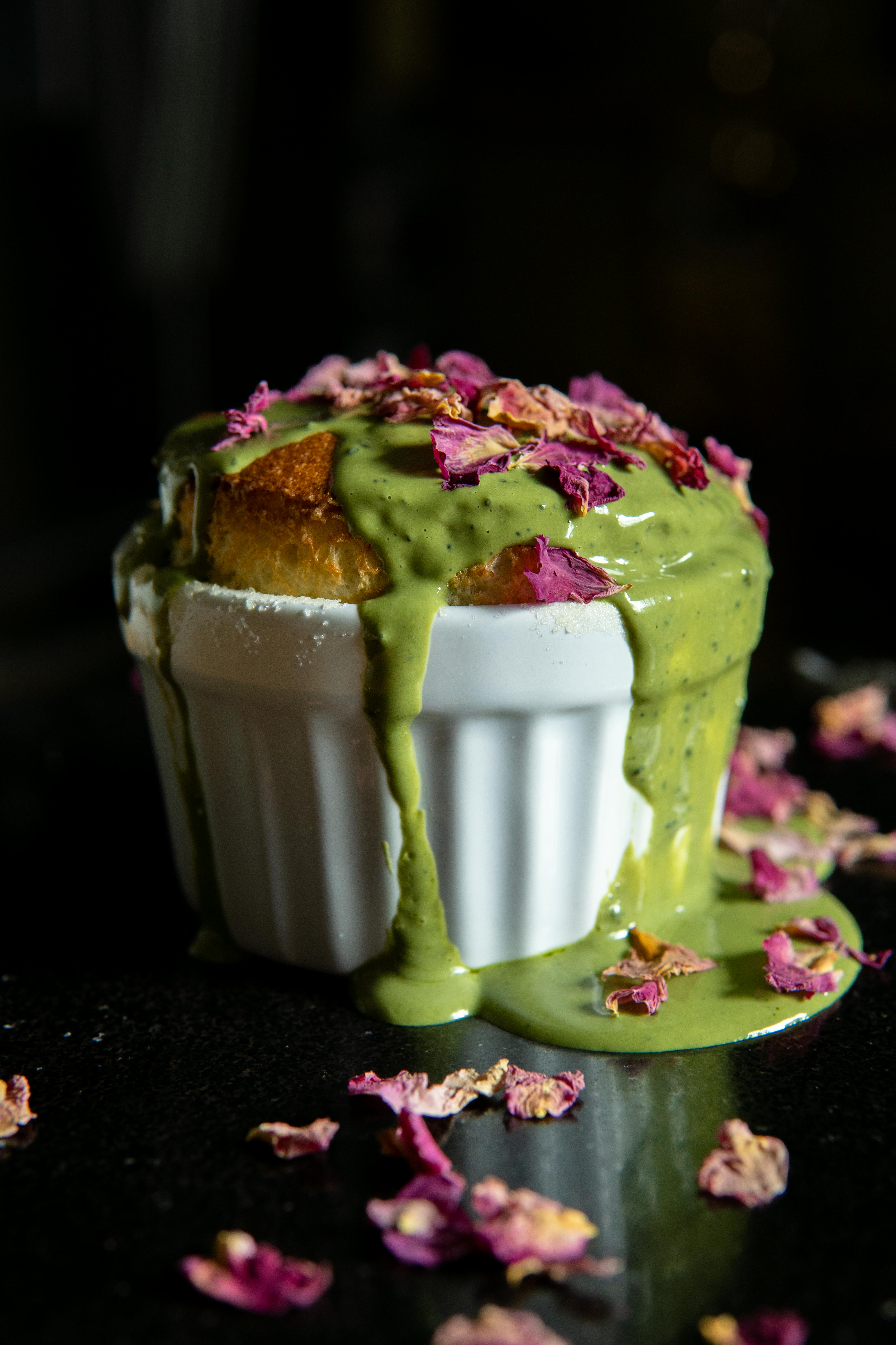 Rich matcha souffle topped with rose petals in a white ramekin on a dark background.