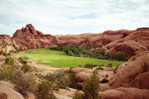 Green Grass Land Surrounded by Brown Rocky Mountains