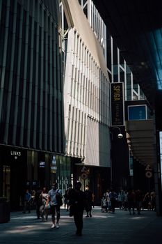 People walking on a busy city street surrounded by modern architecture and sunlight.