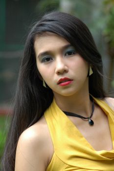 Close-up portrait of a beautiful woman in a yellow dress in an outdoor setting, showcasing elegance and style.
