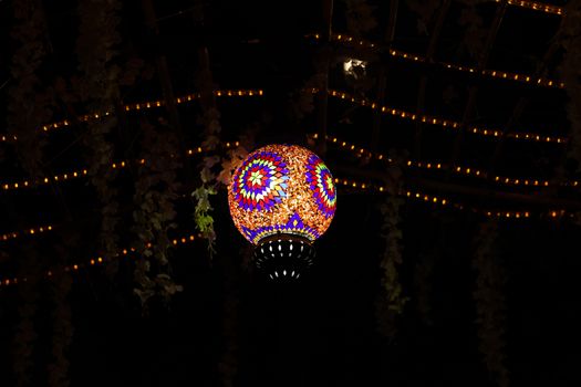 Vibrant mosaic lantern suspended in the dark, surrounded by string lights.