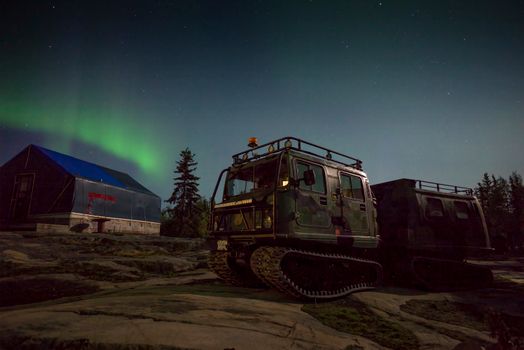 Off-road vehicle parked under aurora borealis in Yellowknife, NT, Canada, at night.
