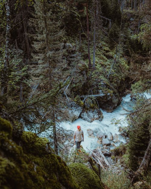 Free A lone hiker in a red hat explores a forest stream surrounded by lush greenery and rocks. Stock Photo