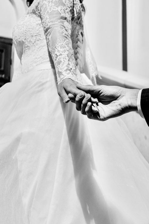 Free Elegant grayscale photo capturing a bride holding hands with her partner, symbolizing love and commitment. Stock Photo