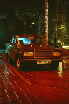 Classic car parked on a rainy city street illuminated by soft streetlights at night.