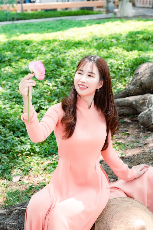Smiling Woman in Peach Long Dress Holding a Pink Flower