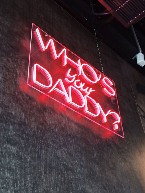 Free Red neon sign reading 'Who's Your Daddy?' in a dimly lit environment. Stock Photo
