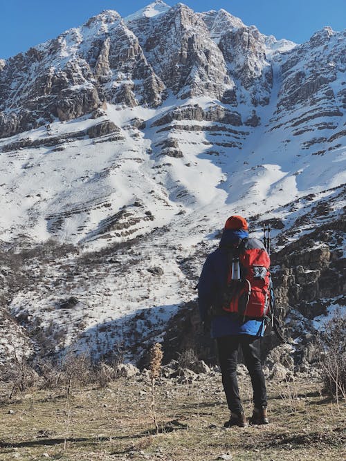 Man in Black Jacket and Blue Backpack Standing on Rocky Mountain