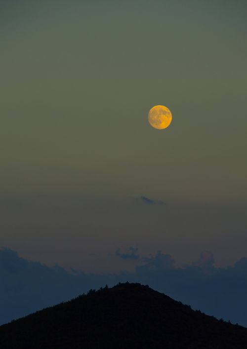 Free A serene full moon rises above a silhouetted hill, creating a tranquil night sky scene. Stock Photo