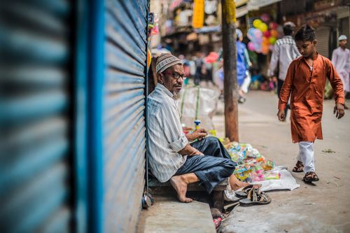 Free An elderly man sells toys on a bustling street as a young boy walks by in traditional wear. Stock Photo