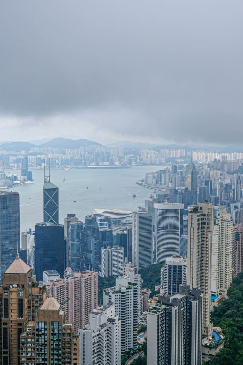 Free Dramatic aerial view of Hong Kong's skyline with towering skyscrapers and a cloudy harbor. Stock Photo
