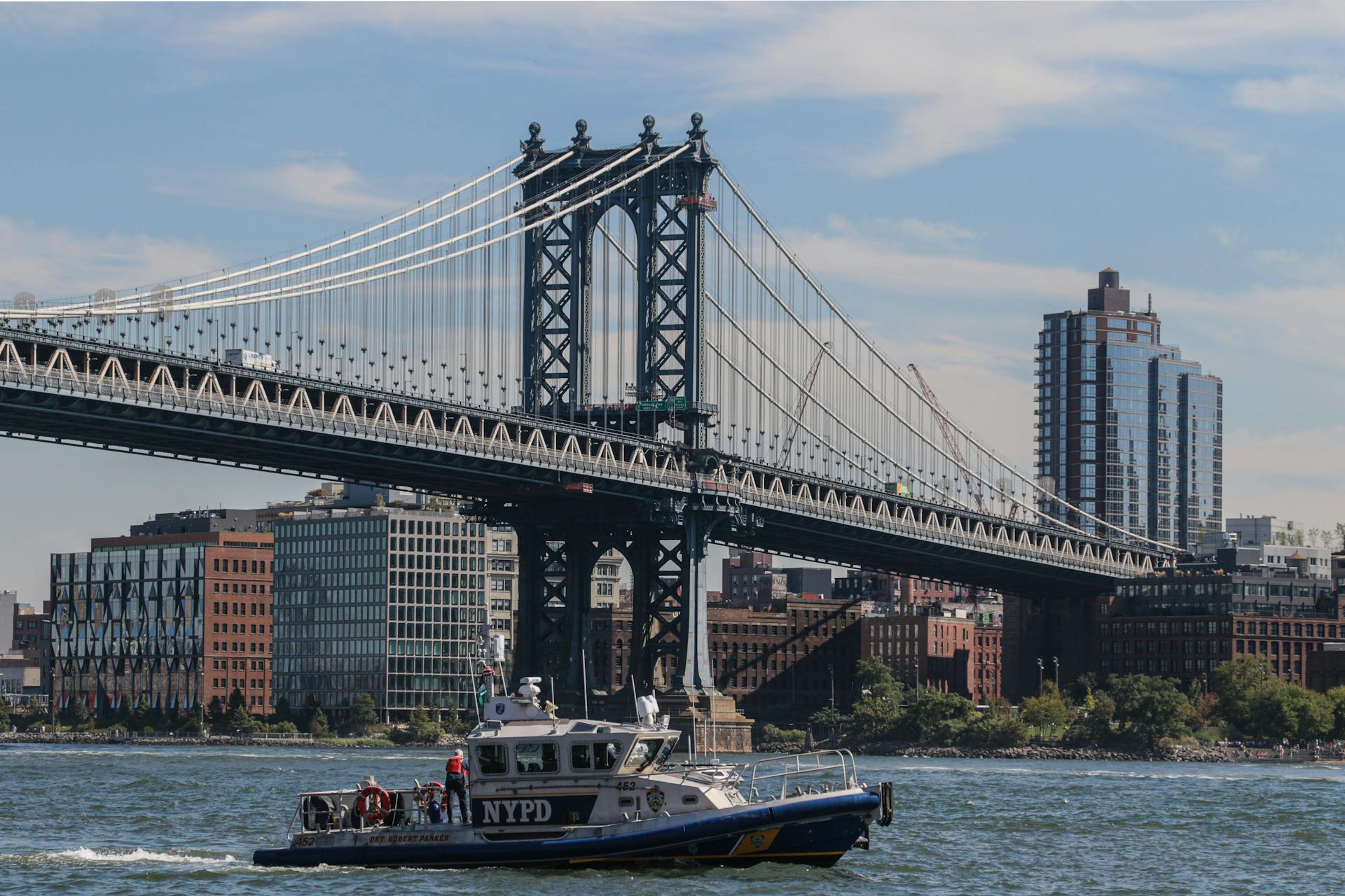 NYPD patrol boat cruising near the iconic Manhattan Bridge on a sunny day in New York City.