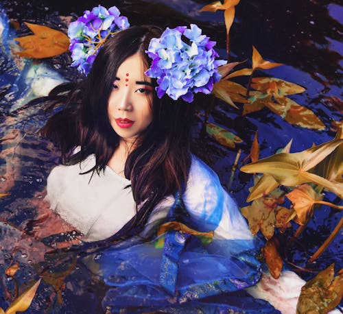 A Woman Wearing a Dress in the Water with Green Leaves