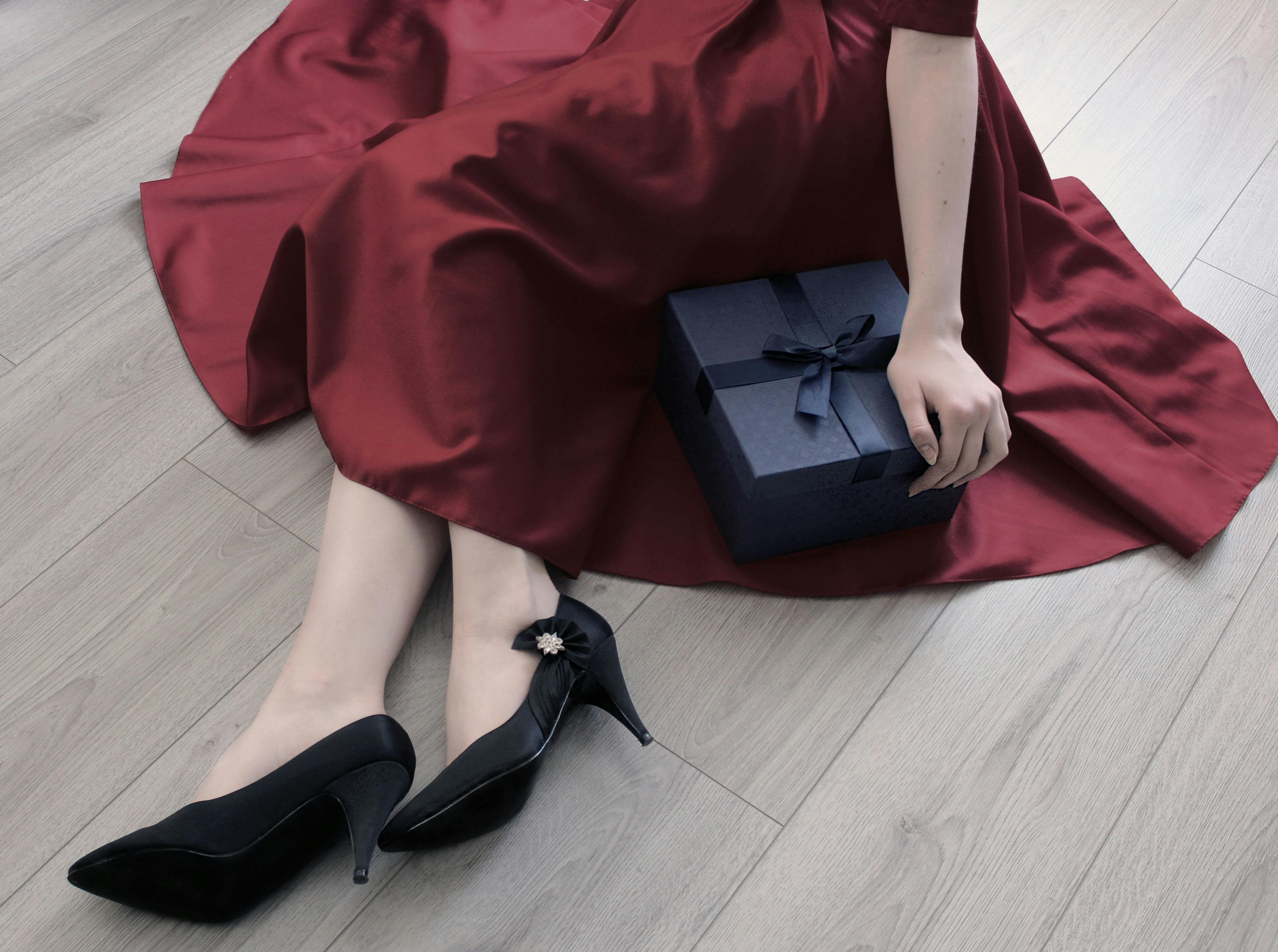 A seated woman in a red dress holding a blue gift box on a wooden floor.
