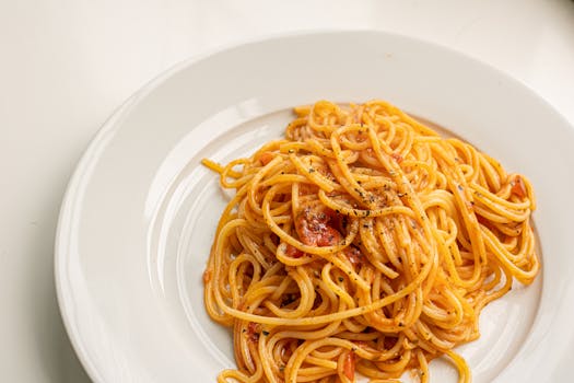 Close-up of spaghetti with tomato sauce on a white ceramic plate, garnished with pepper.