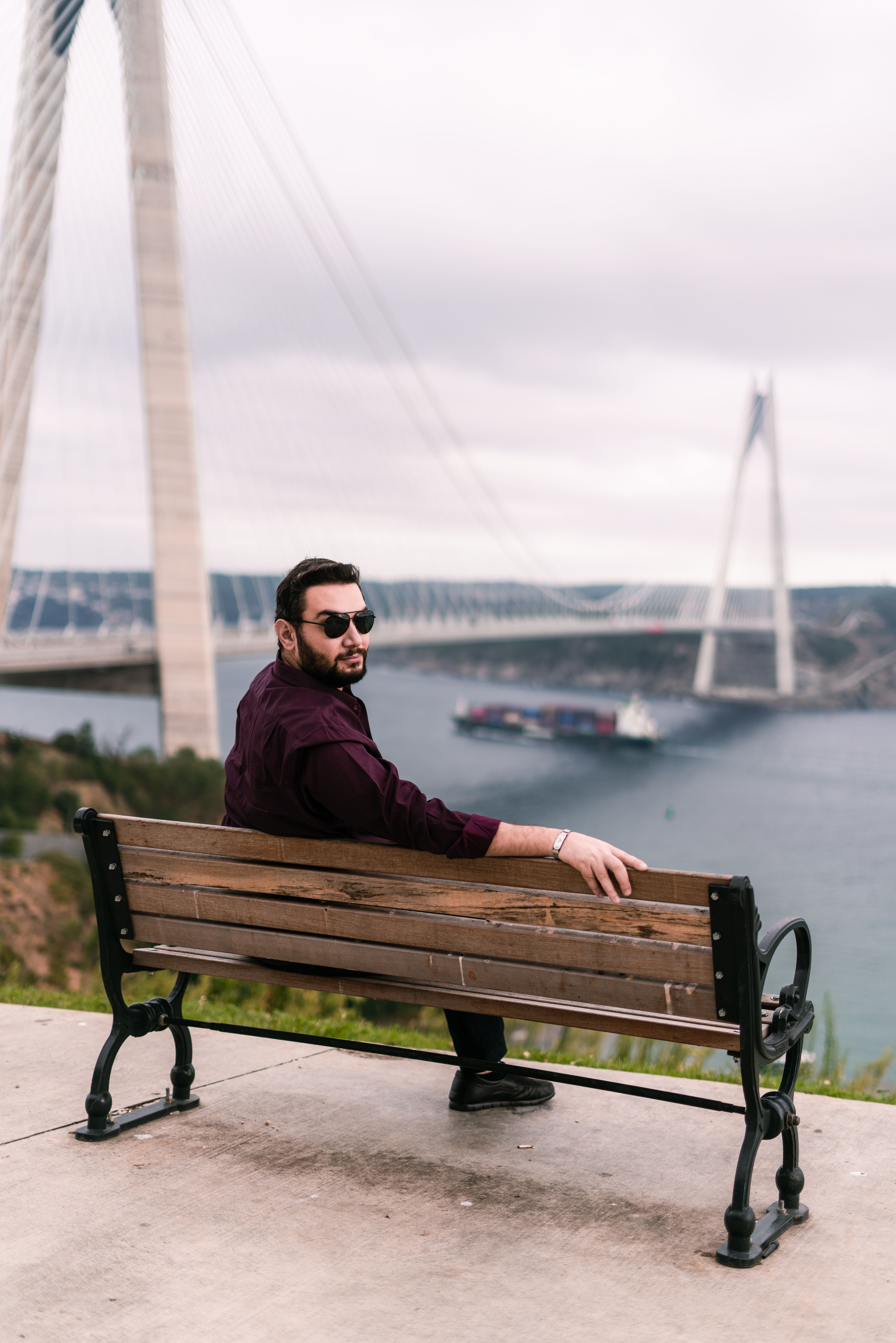 Man sits on a bench with sunglasses, overlooking an iconic bridge in Istanbul, Turkey.