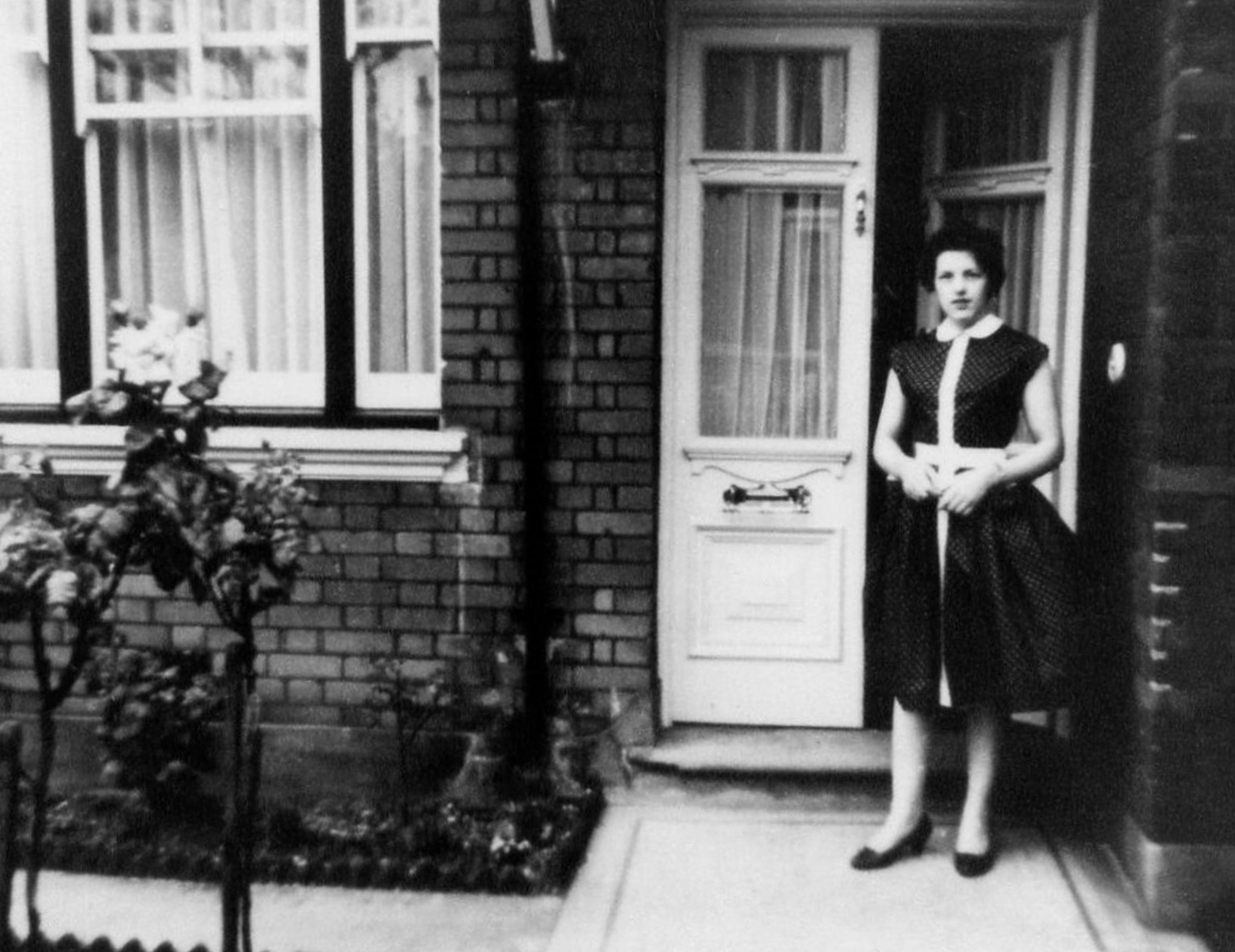 Classic black and white photo of a woman standing in a doorway with vintage charm.