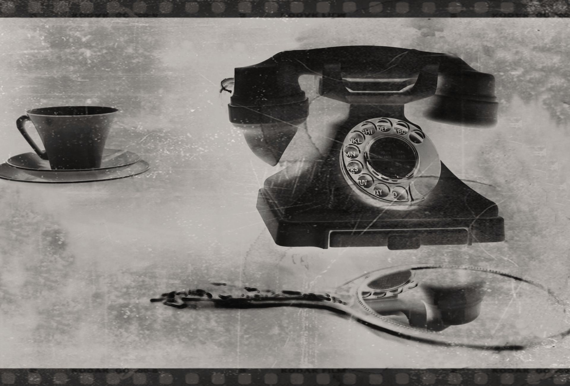 Artistic still life featuring a vintage rotary phone and tea cup in grayscale.