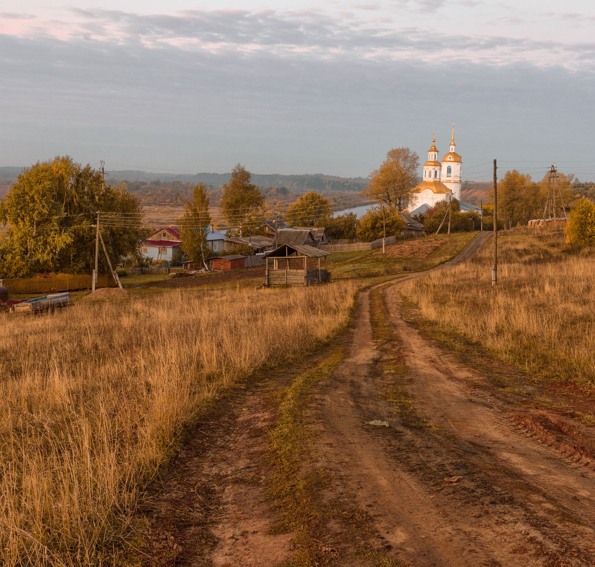 Une route de terre déserte traversant un village rural au crépuscule.
