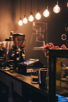 Warmly lit café counter featuring coffee grinder and hanging lights, exuding a cozy atmosphere.