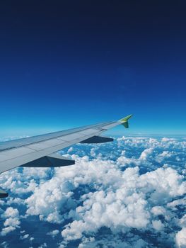 Airplane wing gliding above fluffy clouds under a deep blue sky, offering a serene flight view.