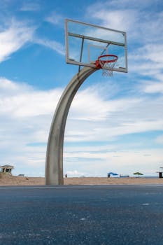 A clear view of a basketball hoop on a beachside court with a vibrant blue sky, showcasing a unique outdoor sports setting.