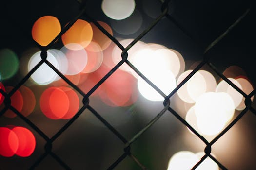 Abstract photo of colorful bokeh lights through a chain link fence, creating a blurred effect.
