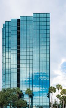 A sleek modern glass building reflecting clouds and palm trees.