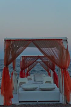 Elegant beach canopy setup with pillows by the sea during twilight, exuding luxury and relaxation.