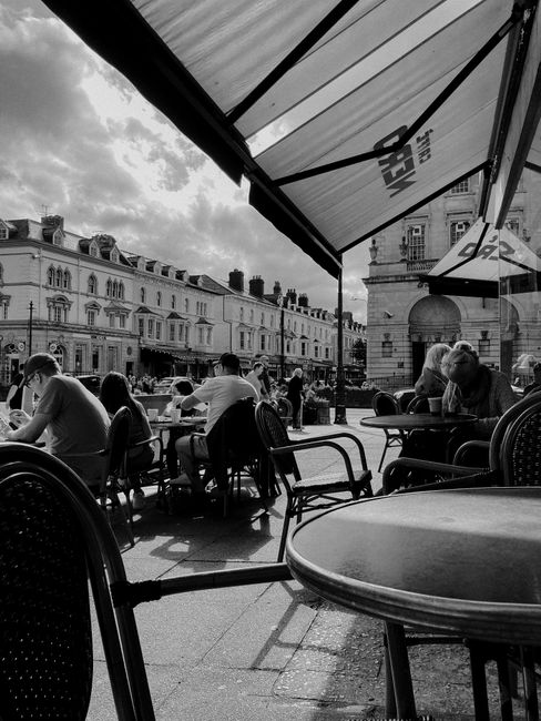 Black and white view of people enjoying leisure time at an alfresco cafe on a historic street.