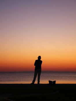 Silhouette of a person overlooking the sea with a vivid sunset sky, reflecting calm and solitude.