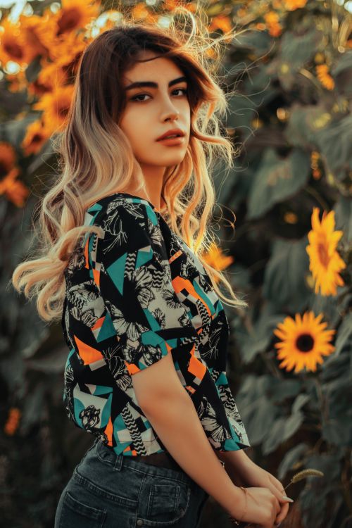 Free A woman with long hair poses in a vibrant sunflower field at sunset, exuding warmth and beauty. Stock Photo